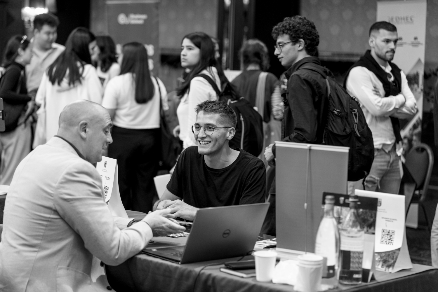 A black and white photograph of two men sitting at a table during a conference with a laptop.