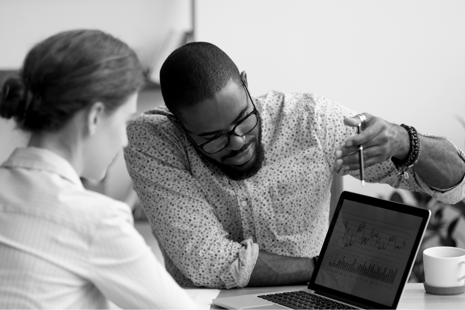 A black and white photo of two people reviewing graphs on a laptop.