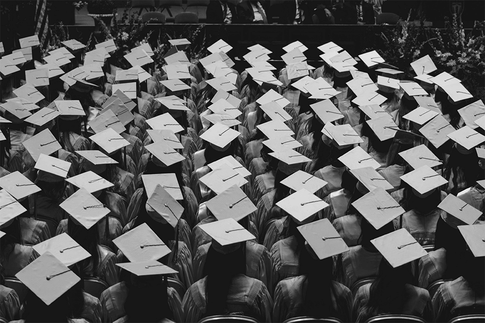 A black and white photo of a group of graduates sitting down wearing their graduation caps.