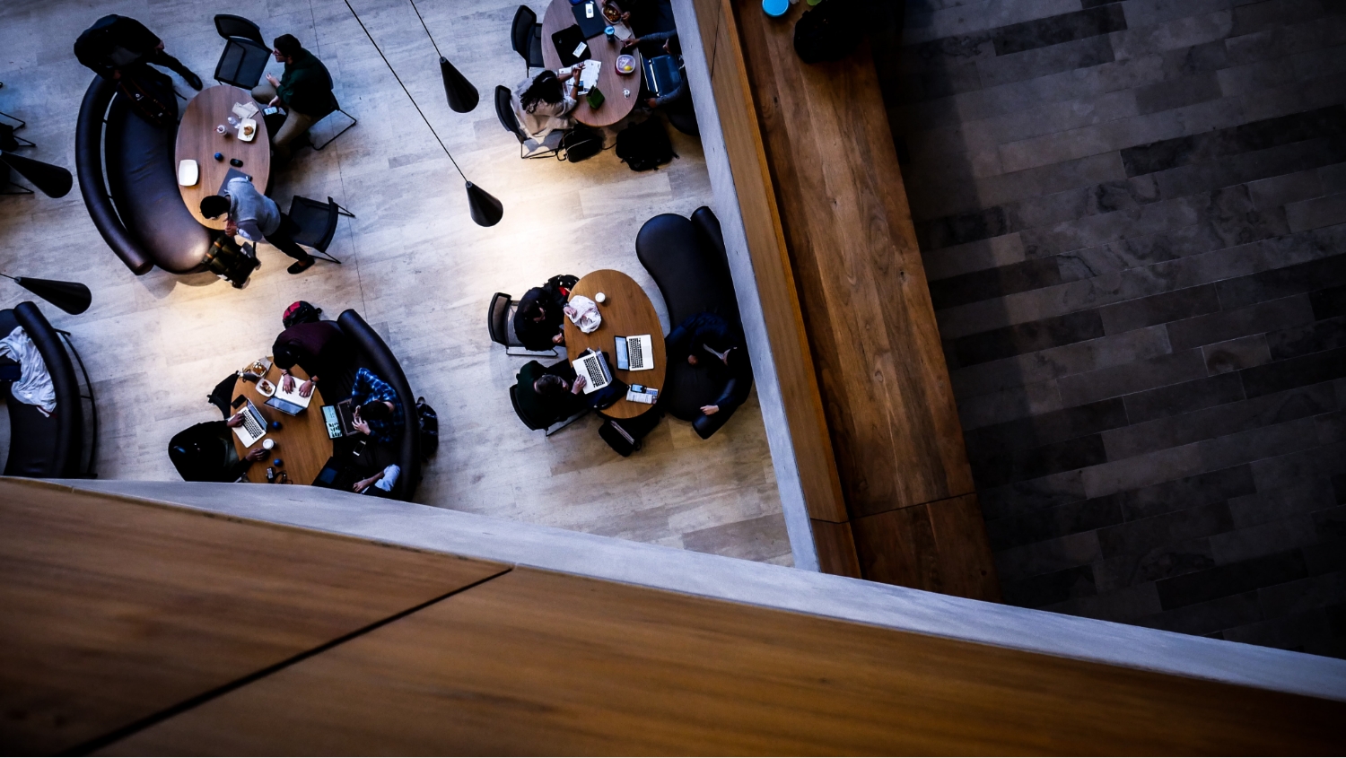 A bird-eye-view photograph overlooking 4 tables with people working with computers at each table.
