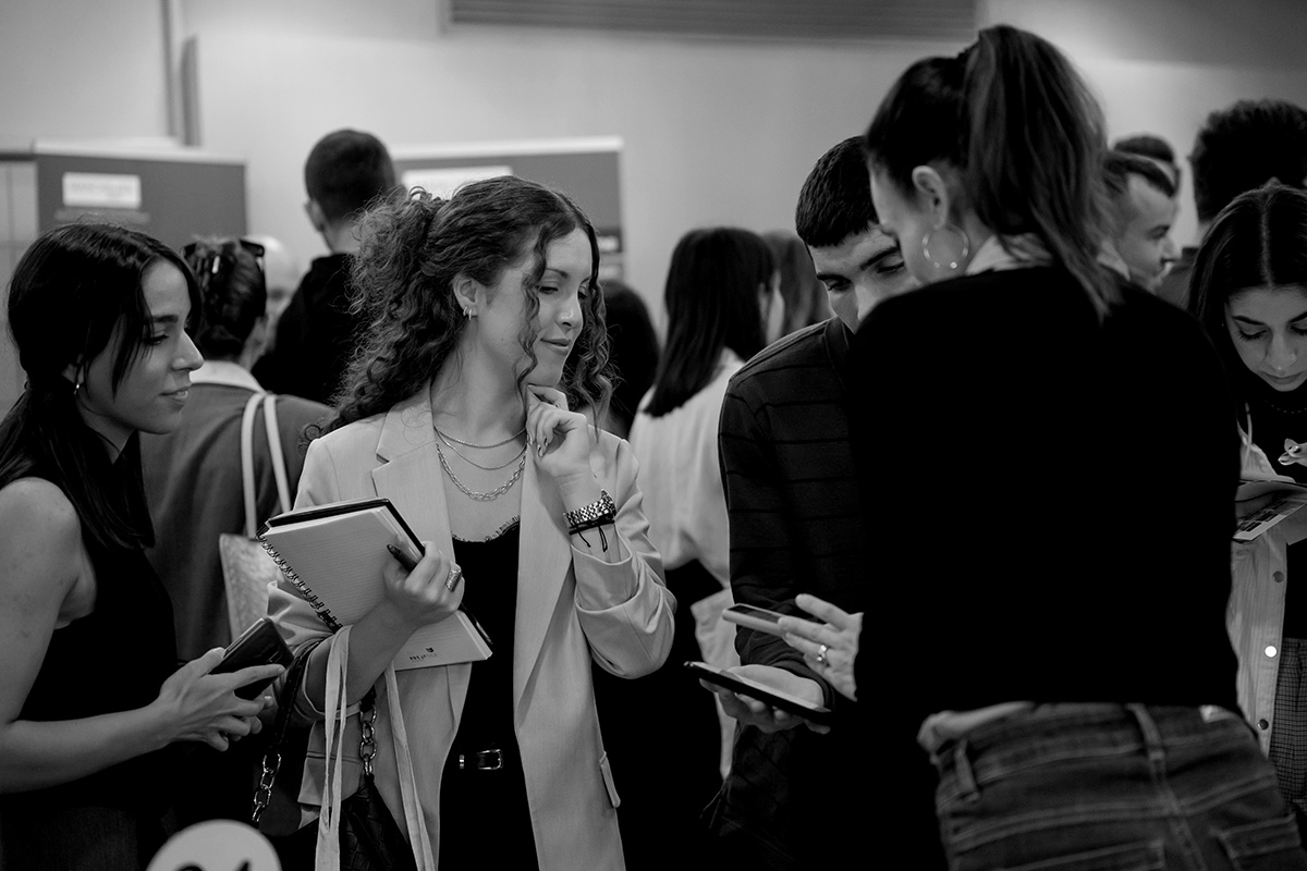 A black and white photo of a group of students gathered in a room, looking at results on a phone.