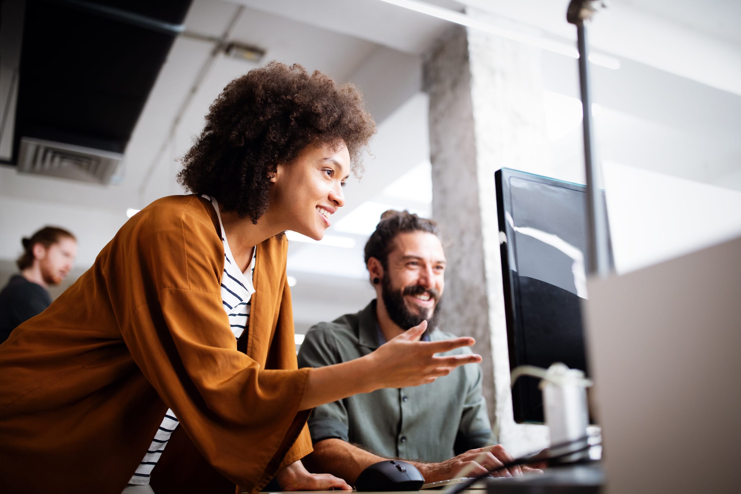 Two employees work together at a computer smiling.