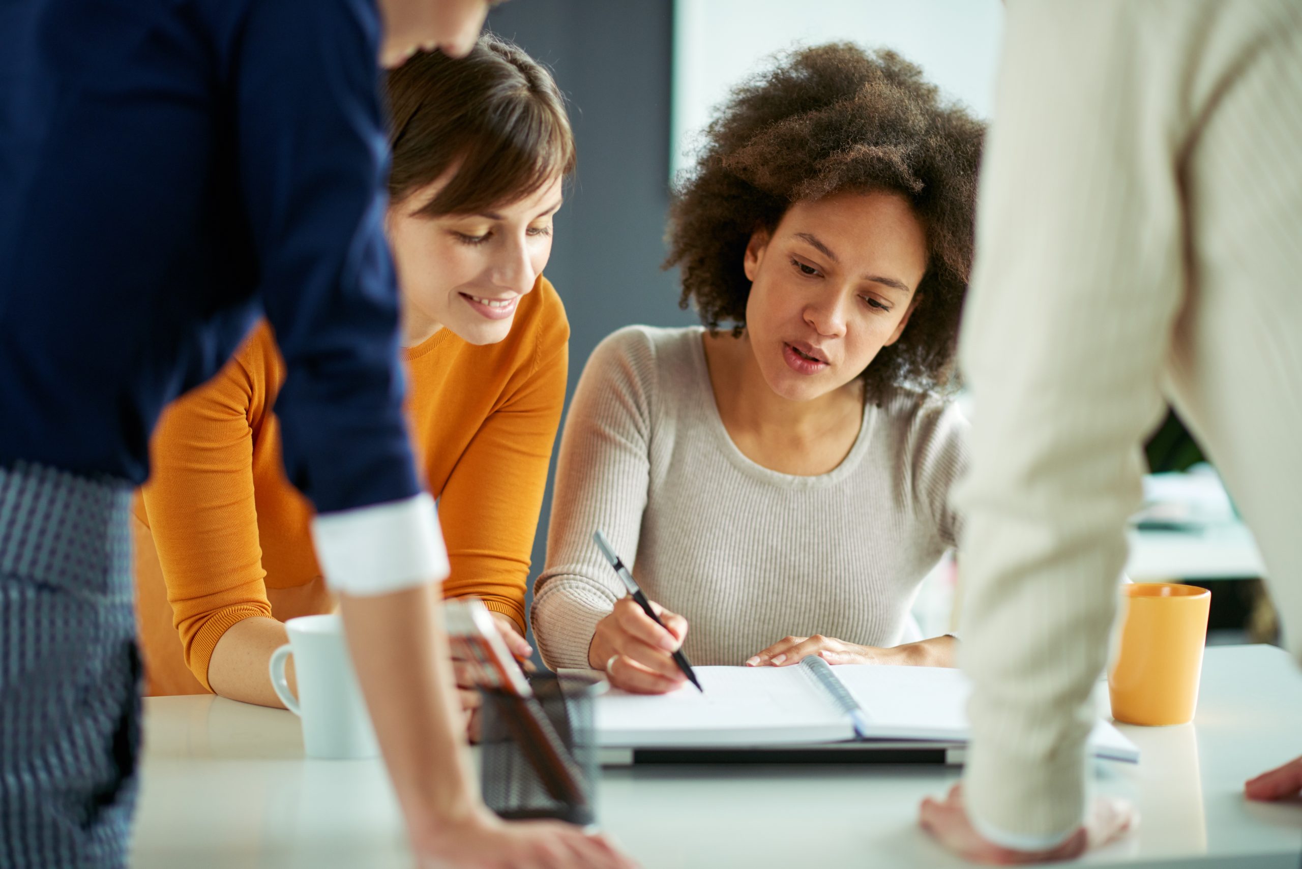 A close-up photo of four employees gathered around a desk whilst one of them writes down some notes in a notepad.