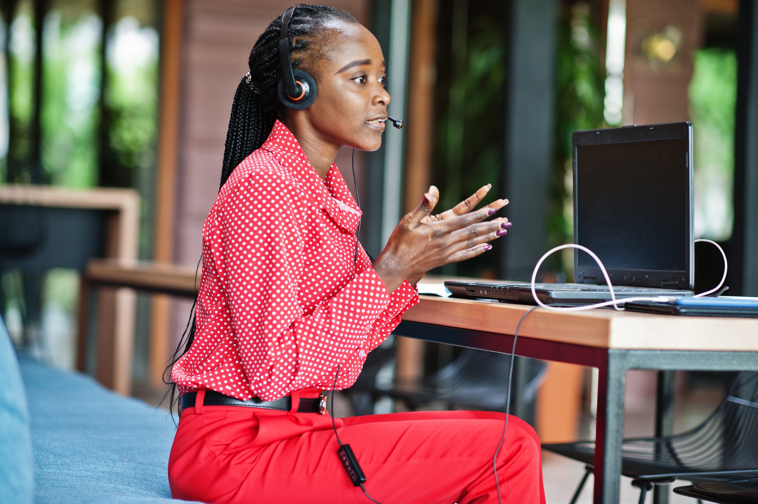 A woman in a checkered red shirt seated with headphones and a laptop.