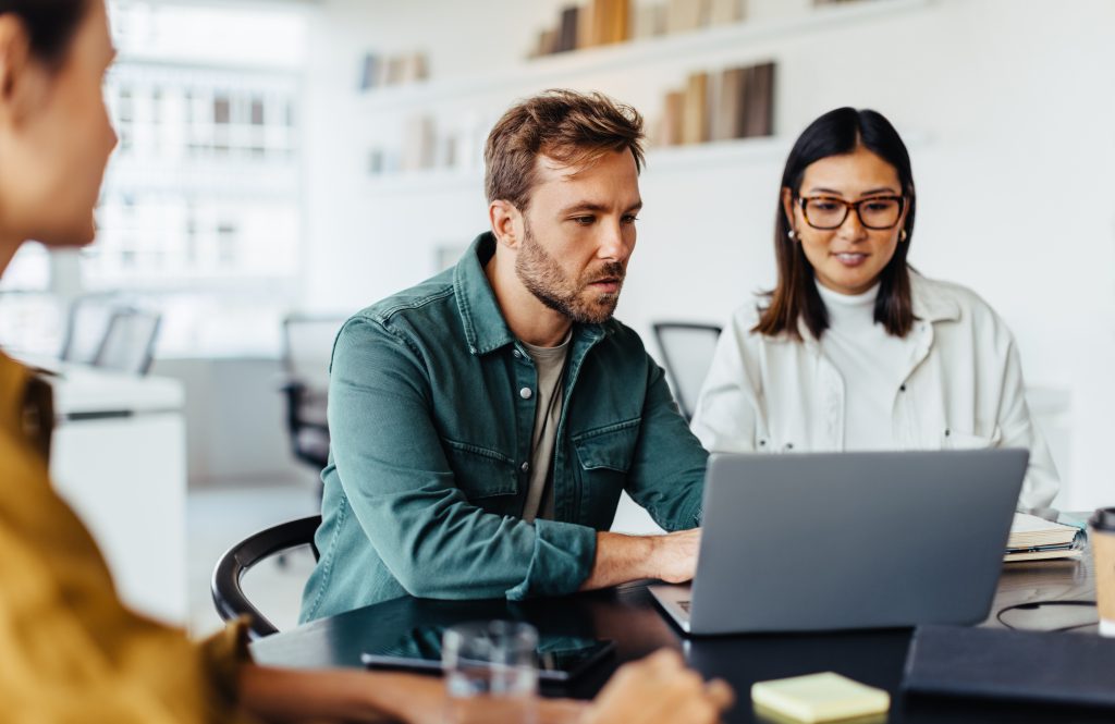 A man works on a laptop while a female colleague watches next to him.