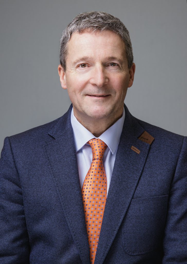 A portrait image of Nunzio Quacquarelli, Founder and President of QS, wearing a blue suit with an orange tie.