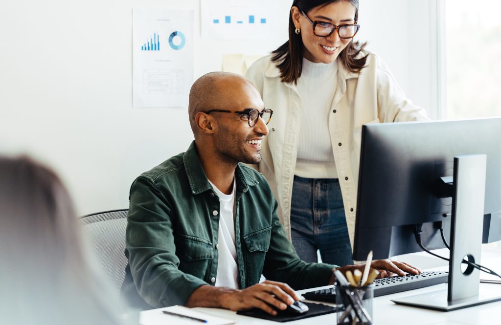 Smiling man in glasses and a chequered shirt works at a computer.