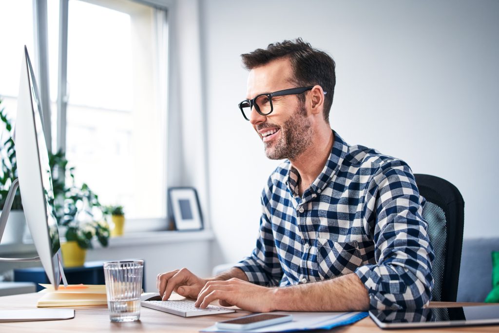 Smiling man in glasses and a chequered shirt works on a computer