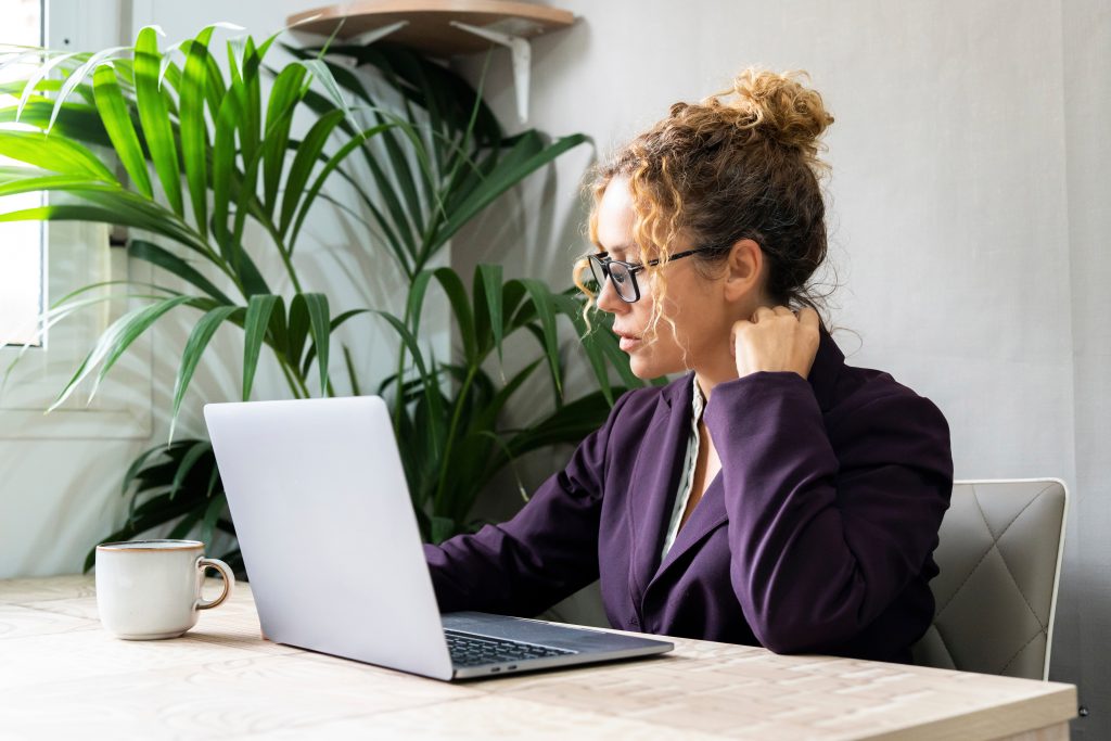 A woman dressed in a purple suit sitting at a desk and working on her laptop.