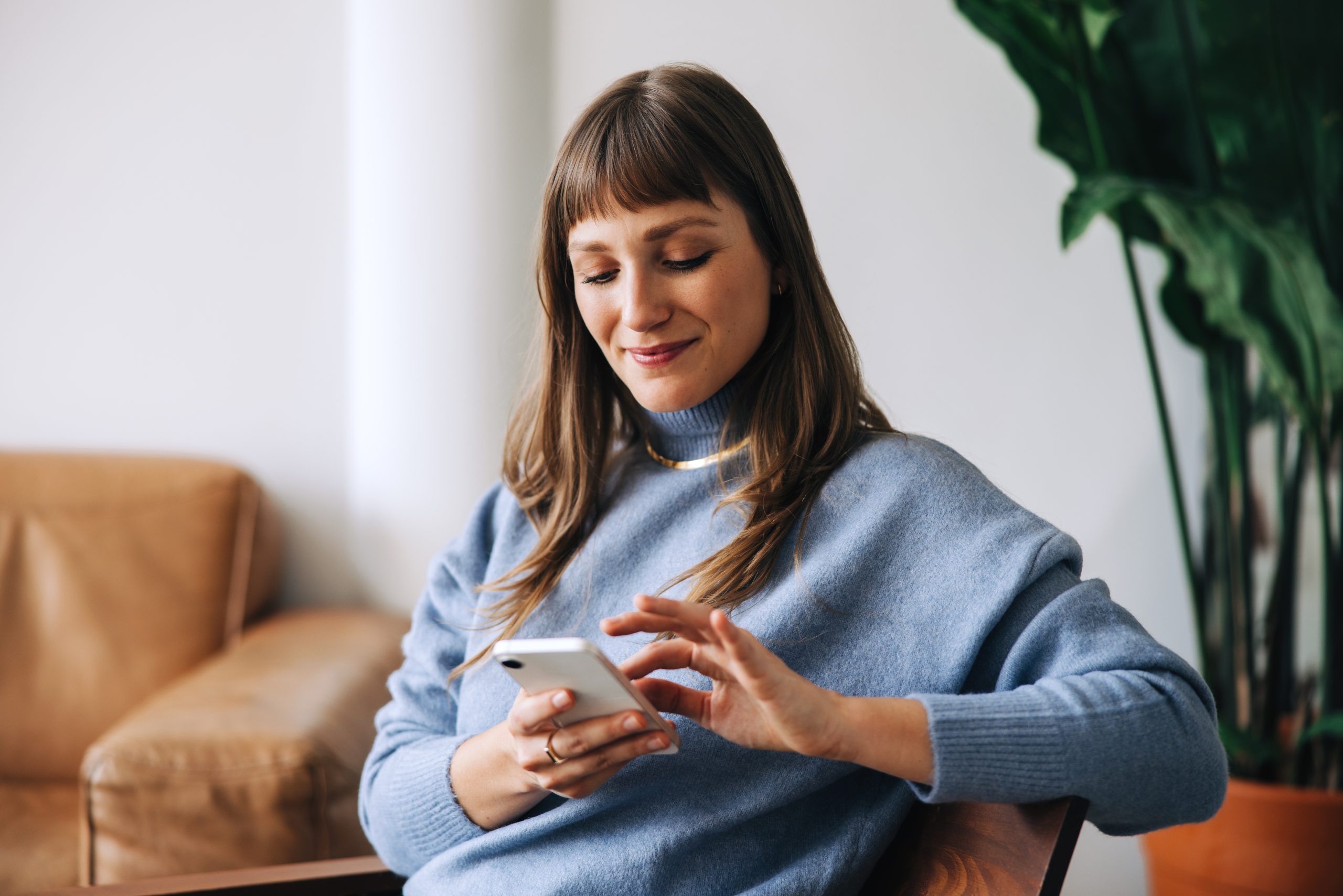 A woman in a light blue sweater using a phonw.