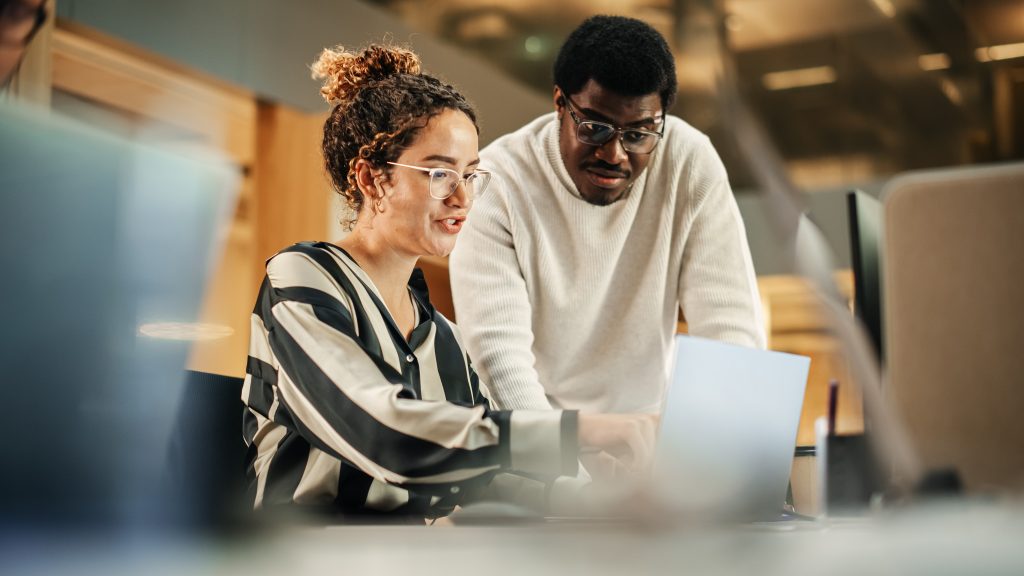 Two employees sitting at a desk and looking at a laptop.