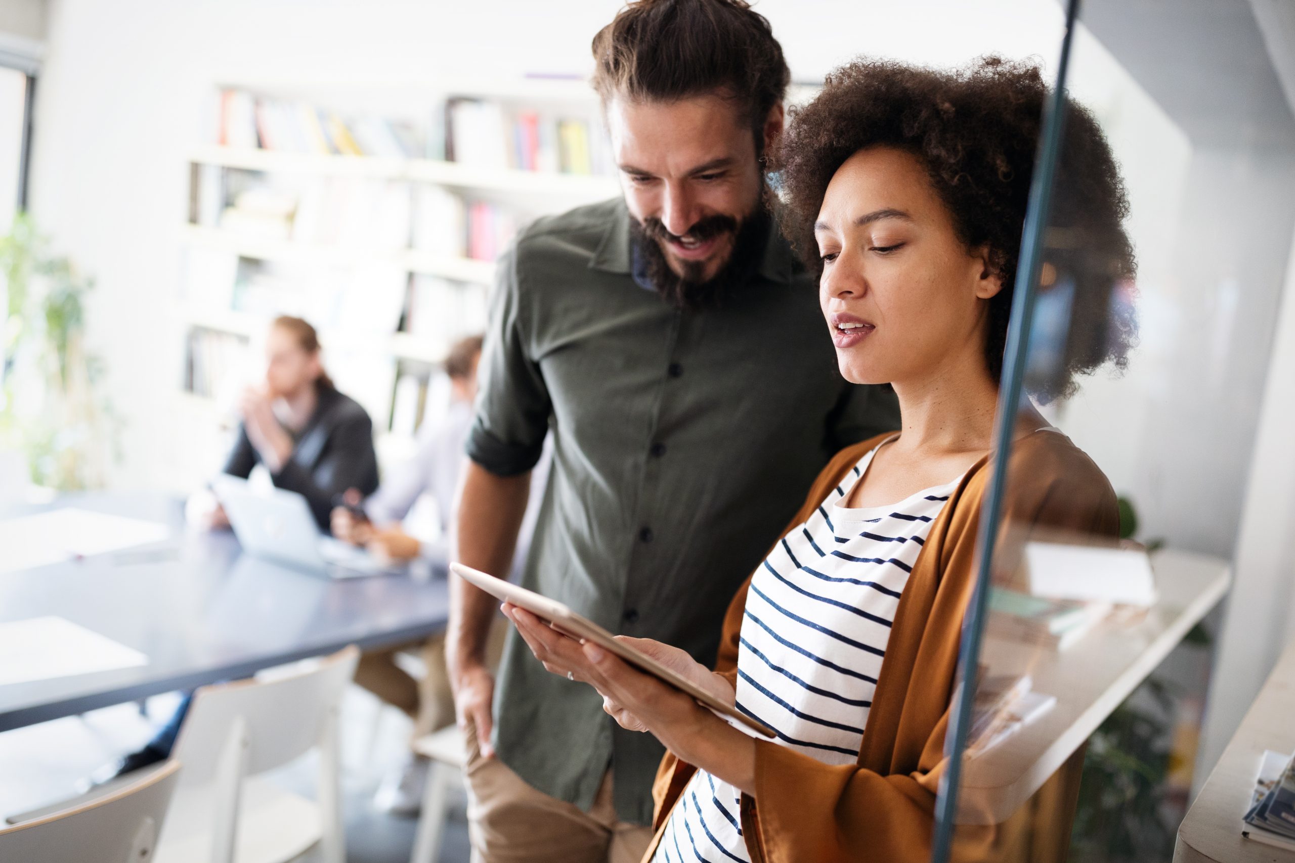 Two employees in an office standing up and looking at a tablet.