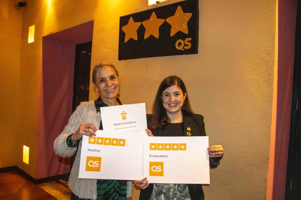 A photo of two women holding pieces of paper from QS that have 5 stars on them for ‘Teaching’ and ‘Employability.