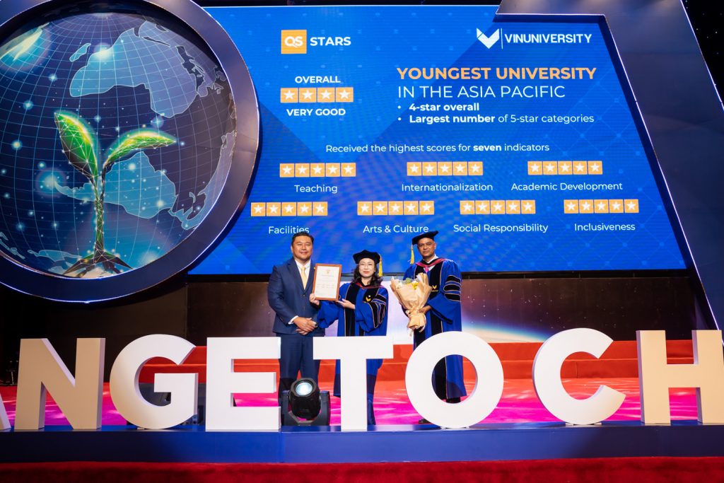 A photo of a student being awarded a diploma with a board reading ‘Youngest University in the Asia Pacific in the back.