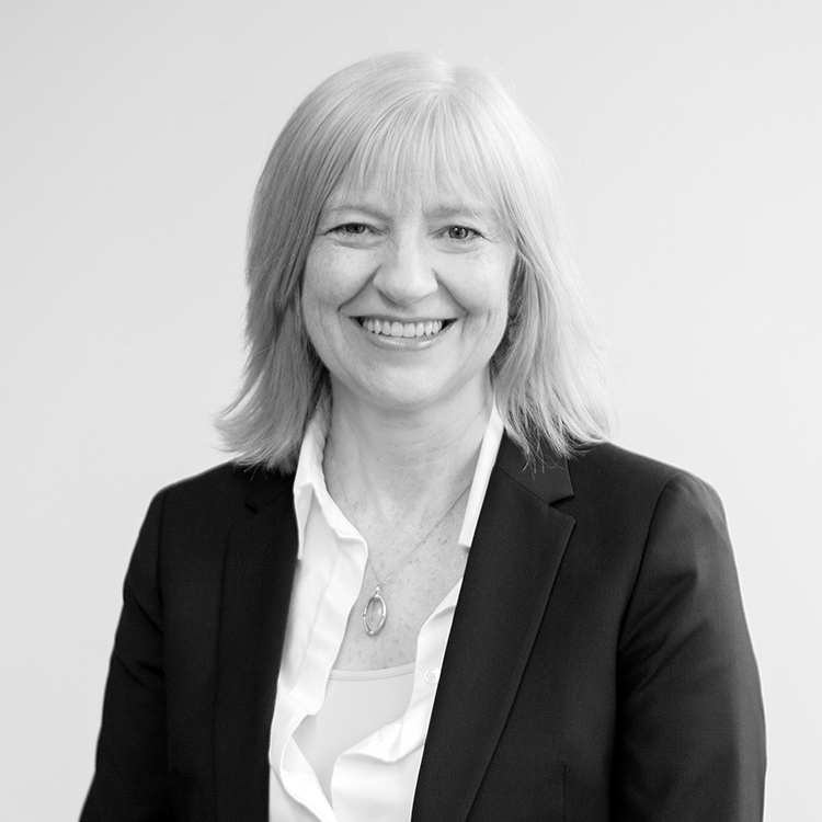 A black and white portrait of Dr Helen Kelly, Principal Consultant at QS, smiling in a dark suit with a white shirt.