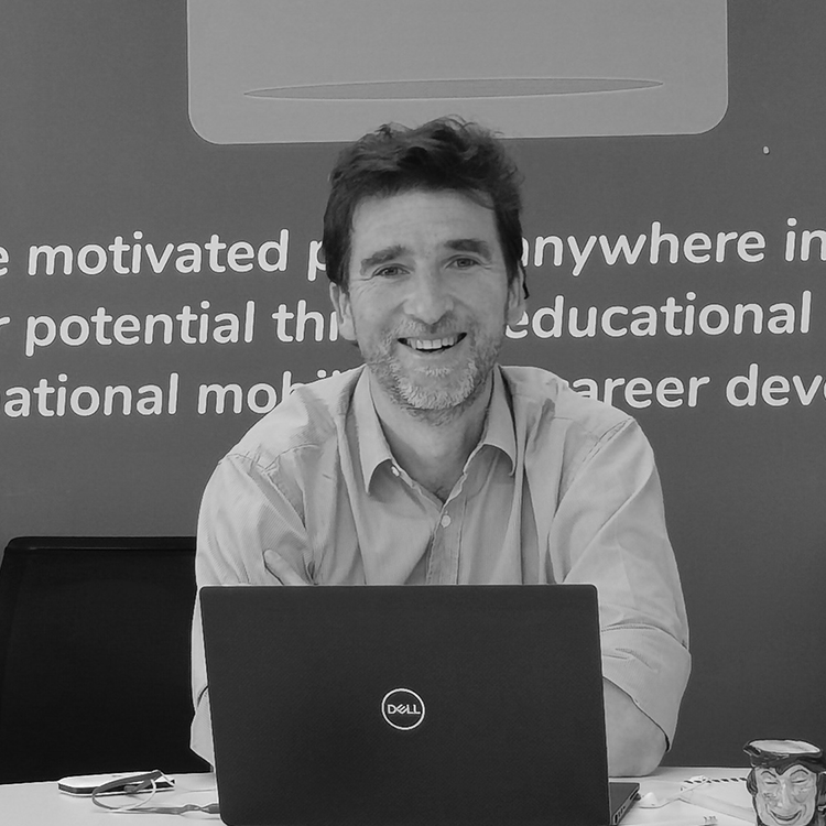 A black and white portrait of Jacques de Champchesnel, Head of Consulting and Insights at QS, sat at a table with a laptop.
