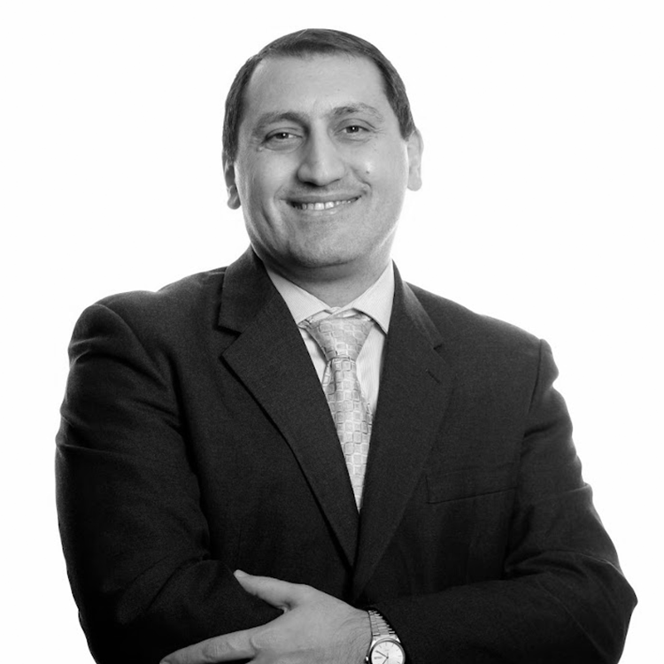 A black and white portrait of Dr Shadi Hijazi, Principal Consultant at QS, wearing a dark suit with his arms crossed.